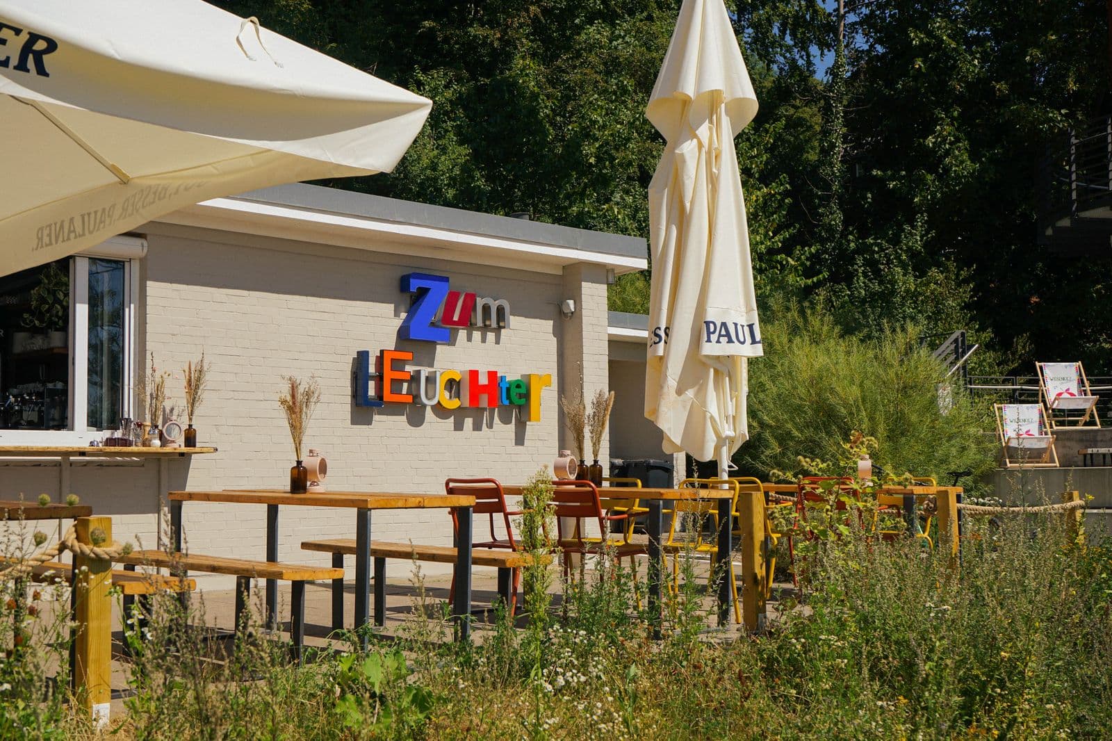 Der Kiosk Zum Leuchter mit bunten Leuchtbuchstaben, Sonnenschirmen und Wildblumen